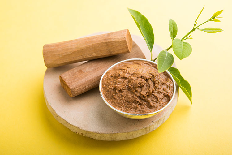 A bowl of sandalwood paste placed next to a couple of sandalwood sticks.