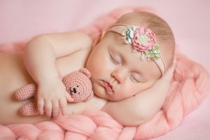 Adorable infant wearing a floral headband sleeping with her stuffed to