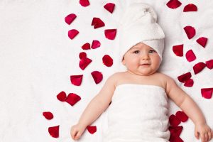 Baby wrapped in white towel lying on bed, surrounded by rose petals!