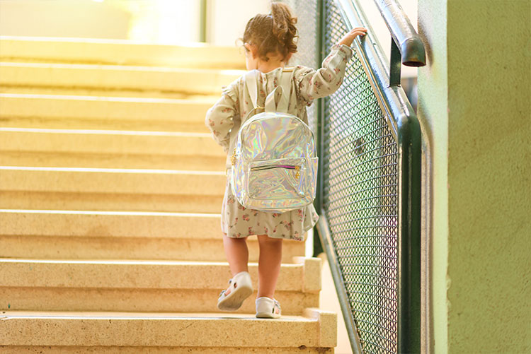 A girl wearing a casual backpack climbing up the stairs.