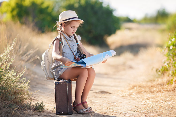 A young girl sitting on her travel suitcase while she looks at a map.