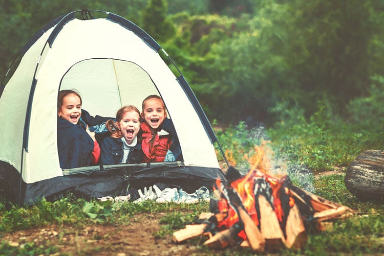 Three young girls sitting inside a tent in the woods with a bonfire!