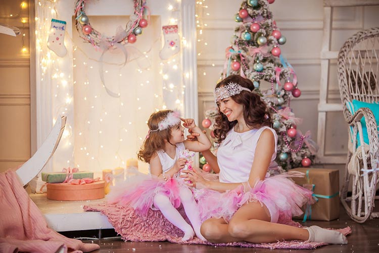 Adorable daughter with mother wearing matching pink puffy skirts set against a Christmas tree background!
