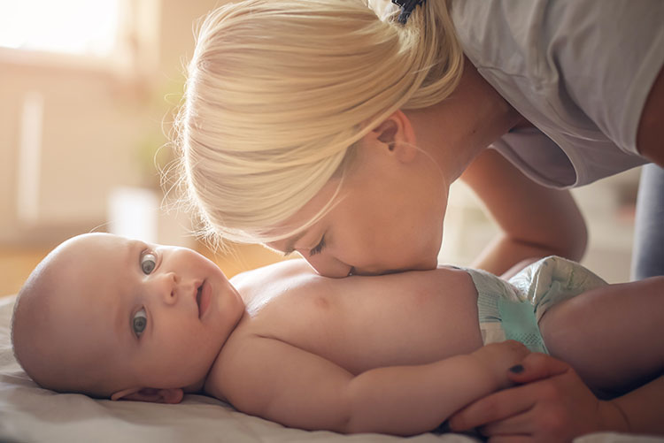 A newborn looks at the camera while his mom gives a kiss on his tummy.