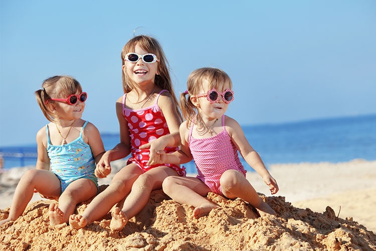Three girls, wearing swimwear, playing on the beach.