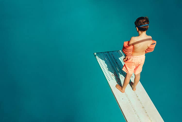 A young boy gazing into the pool from a swimming board.