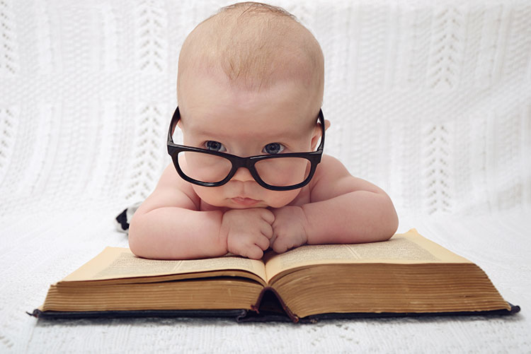 A boy wearing glasses placed in front of a huge book.