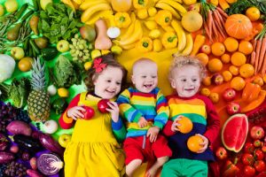 Three toddlers lying down amidst fresh fruits and vegetables