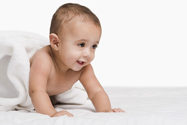 A baby boy crawling on the bed.