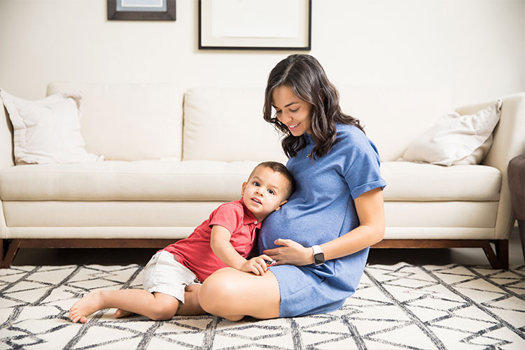 A young boy resting his head against his mother's baby bump.