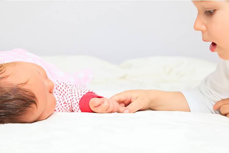 A young boy holding his newborn sister's hand.