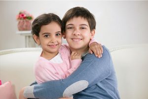 A young boy giving his little sister a hug.