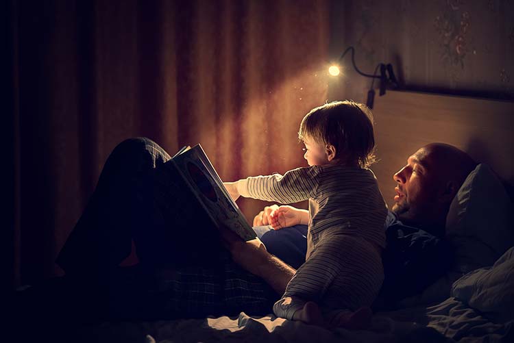 A boy pointing at a story book his father is reading.