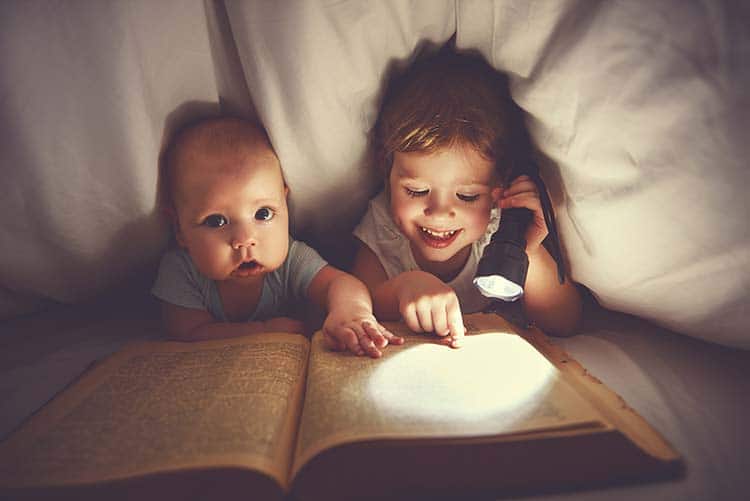 Two young boys reading a story under a blanket.
