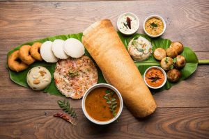 South Indian meal laid out on a banana leaf, including - dosa, uttapam, idli, sambar, upma, semolina halwa, and chutneys