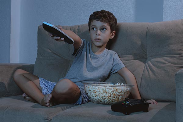 A boy watching TV while munching on popcorn.