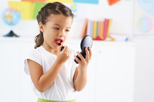 Little girl wearing red lipstick looking in the mirror