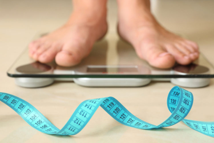 Person checking the weight on a weighing scale with a measuring tape lying around