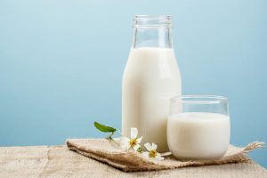 A glass and bottle full of milk placed on a table with flowers