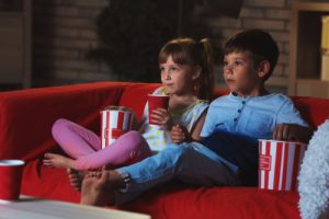 Two young kids watching a movie while eating popcorn