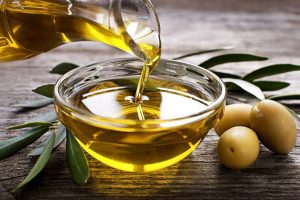 Bottle pouring olive oil in a glass bowl, with olives kept at the side.