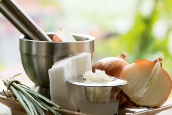 A tray with halved onions, coconut oil, lemongrass, cotton pads, and mortar pestle. 