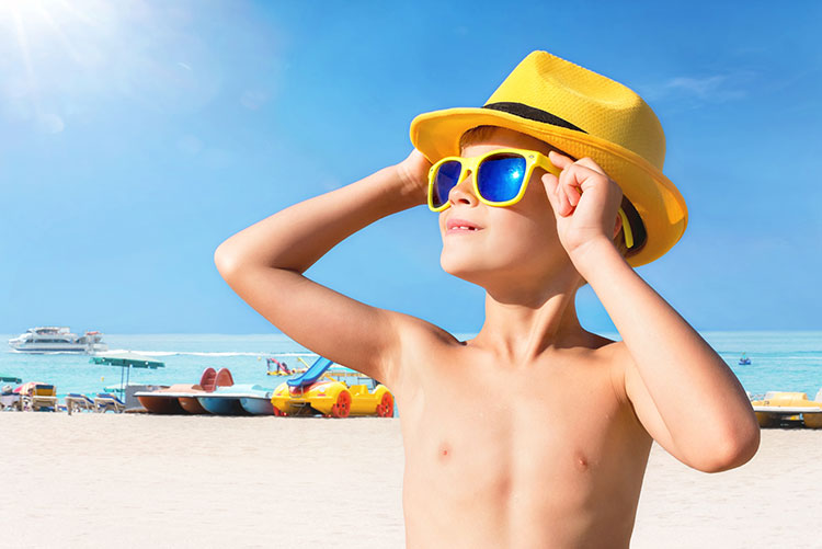 A boy on the beach wearing a pair of sunglasses and a hat.