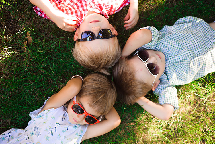 A group of kids wearing sunglasses lying adjacent to each other.