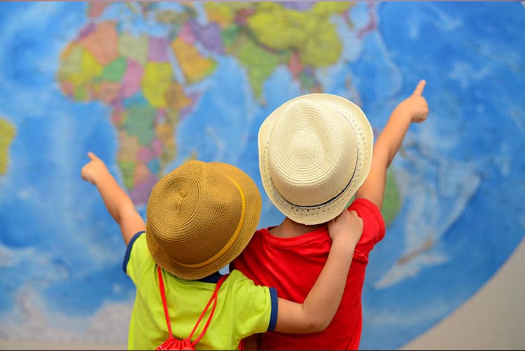 Young boys wearing fedora hats pointing at a giant globe!