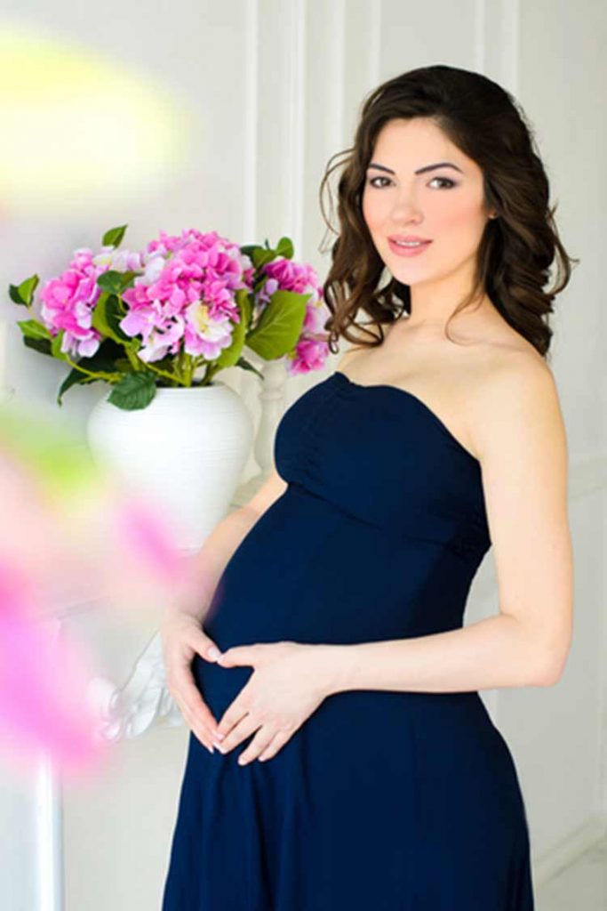 Pregnant woman in a strapless gown holding her belly