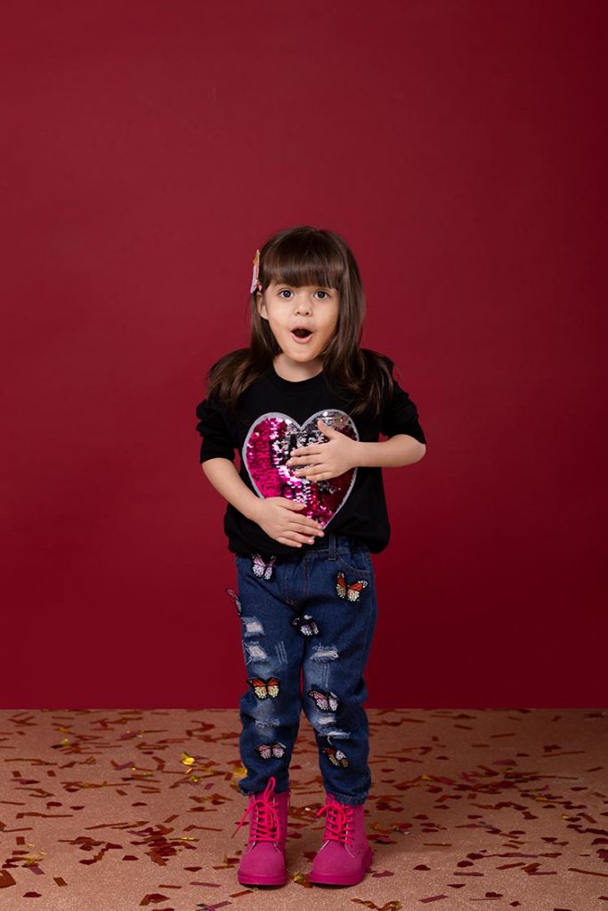 A girl playing with the sequins on her sweatshirt.