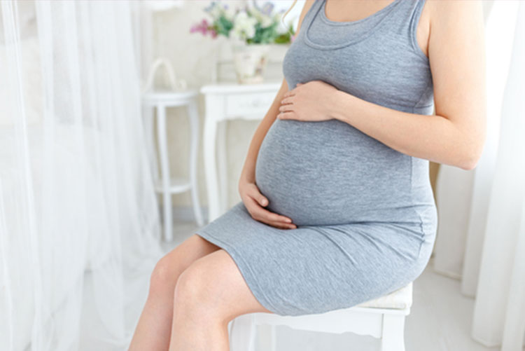 Pregnant woman in a stretchy dress sitting down and holding her belly