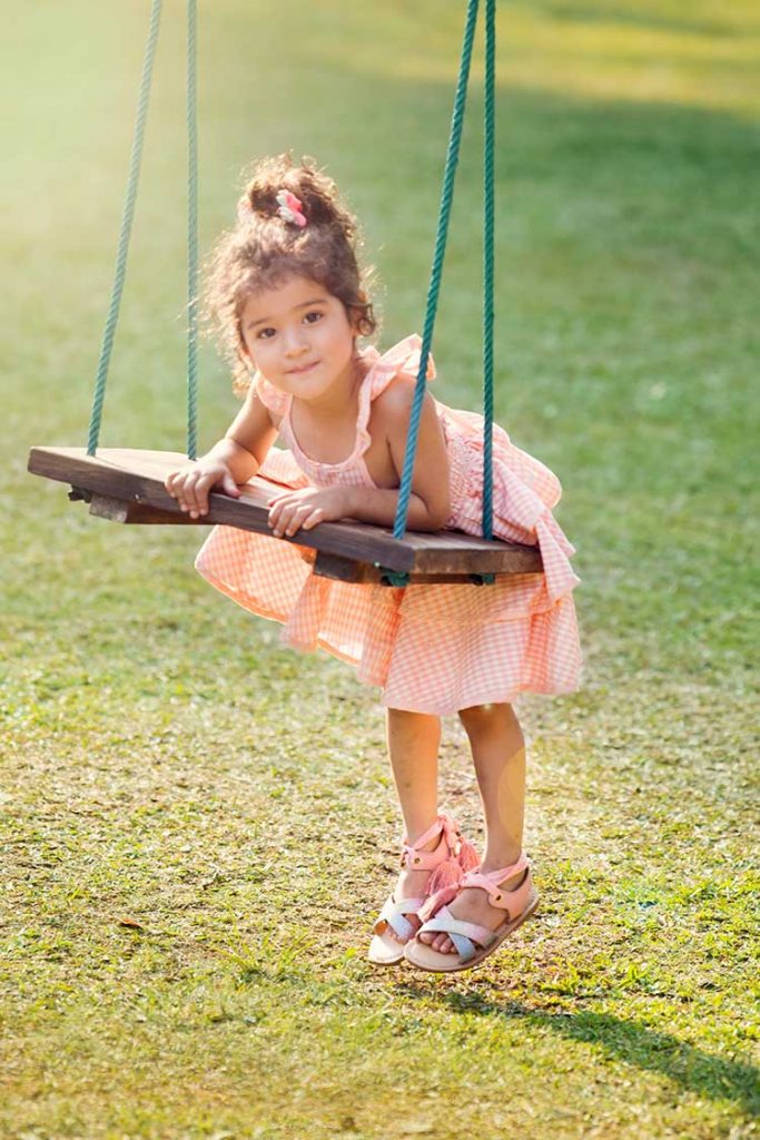 A girl wearing a summer dress while playing on a swing.