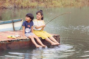 Two kids sitting on the deck by a lake.