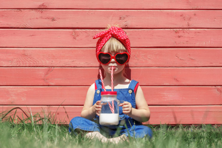Little girl in dungarees and sunglasses sipping milk from a mason jar