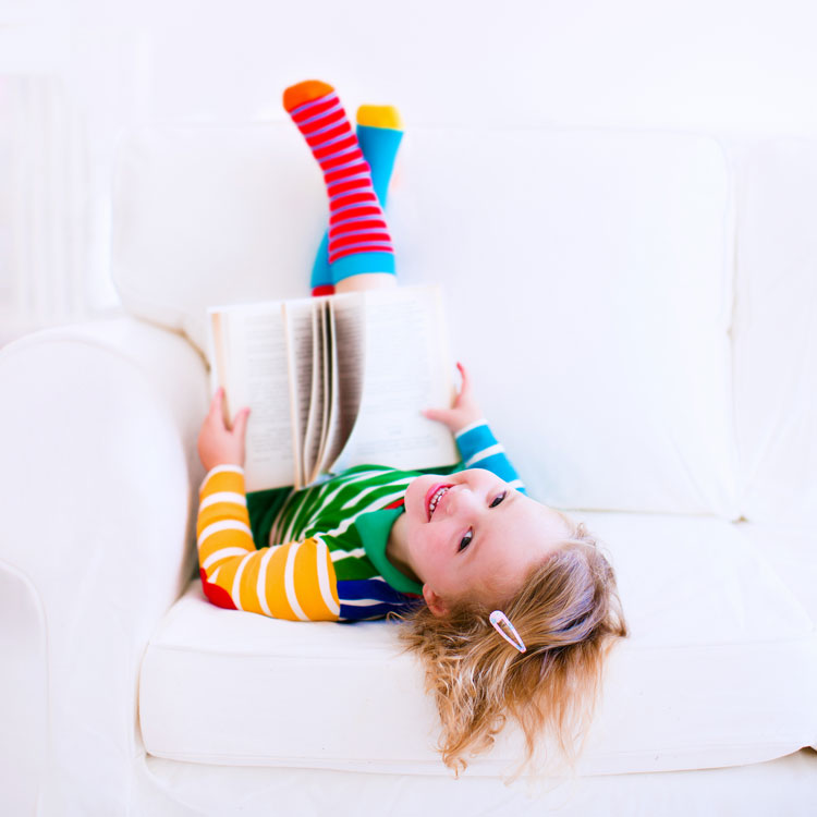 A girl sitting upside down on the couch while wearing a pair of mismatched socks.