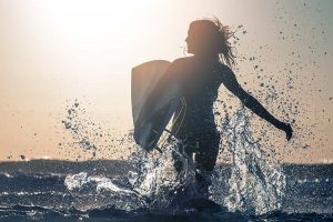 A happy lady wading through the water with a surf board.