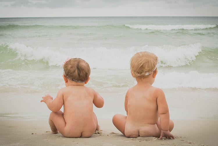Two babies made to sit facing the ocean.