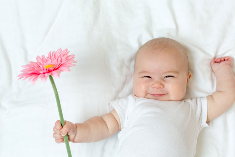 Infant lying on a bed holding a flower in his hand!