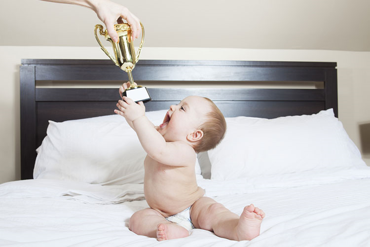 Infant excitedly receiving a trophy while sitting on the bed!