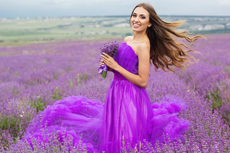Woman wearing a lavender dress, holding purple orchids, standing in a lavender field.