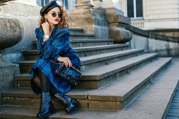 Pretty lady posing on the street wearing a blue tartan patterned dress, black retro sunglasses, and black boots and beret!