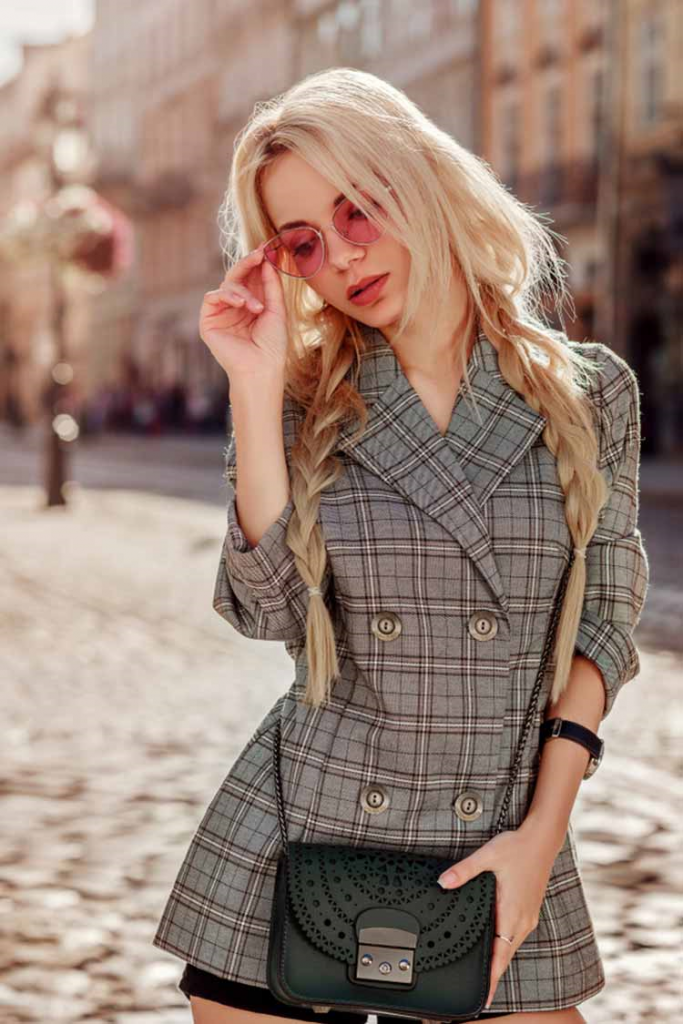 Beautiful, blonde woman sporting a tartan blazer and carrying a deep green clutch and pink retro sunglasses!