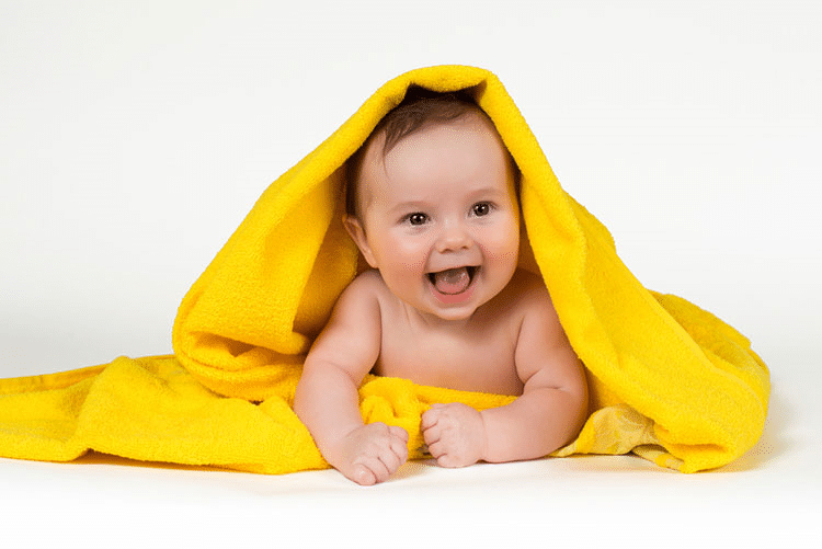 Baby lying on bed, covered from head to toe in a yellow towel!