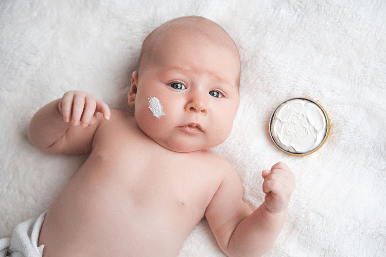 Infant lying on the bed with a smudge of lotion on his right cheek!