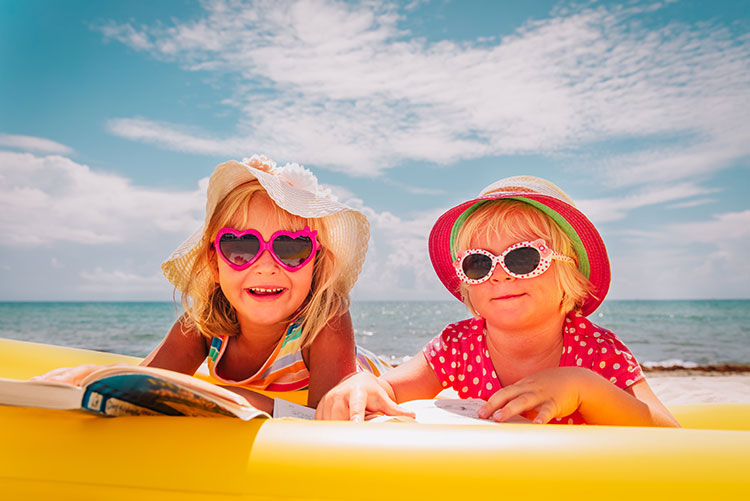 Two young girls wearing cool sunglasses, lying on the beach!