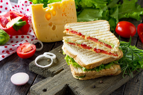 Vegetable sandwich placed on a chopping board with veggies and cheese