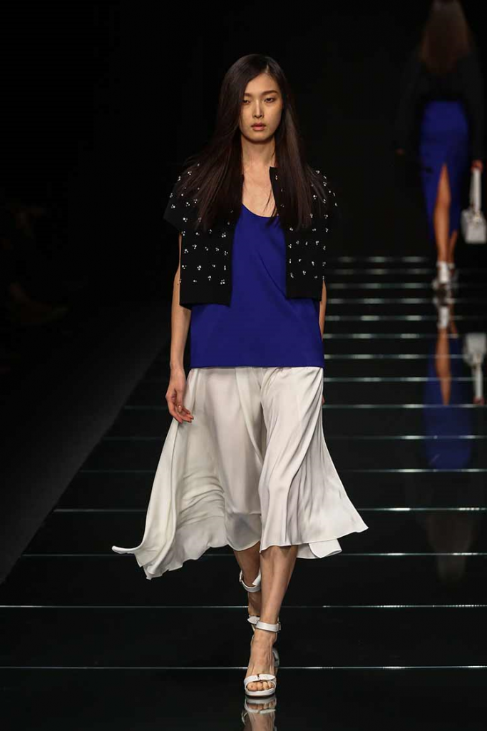 Model walks the ramp wearing a Classic Blue top paired with a black shrug and white skirt and shoes!