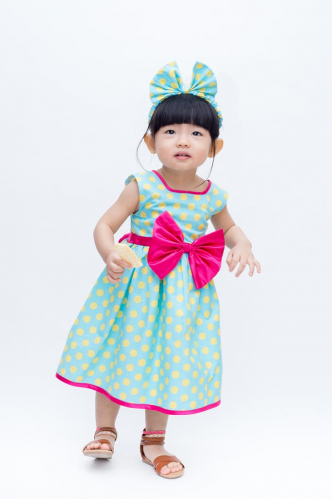 Cute young girl in a blue-yellow polka dot dress with a pink centre-bow and headband!