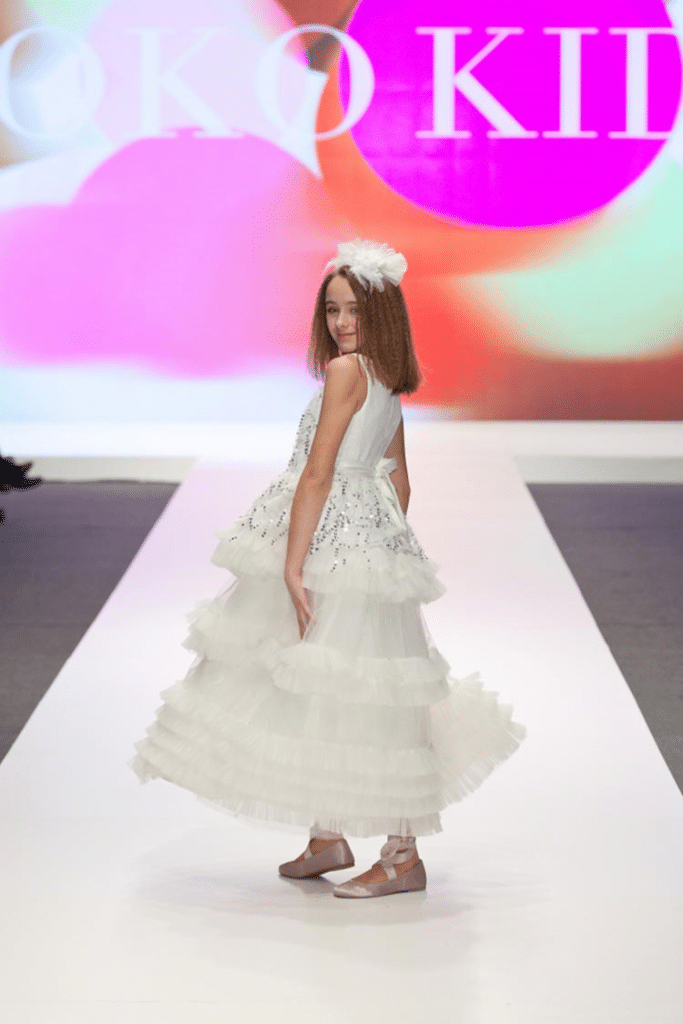 Pretty girl twirling on a ramp in a dreamy, lace white dress with white headgear!